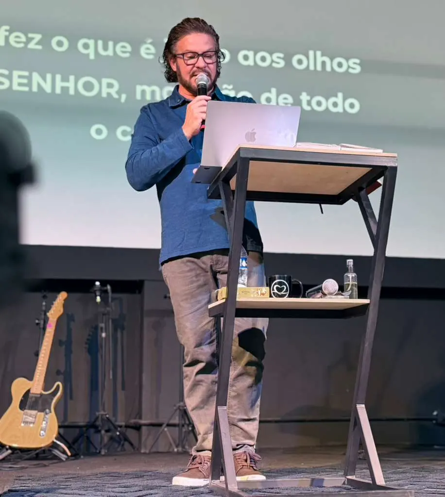 Pr. Robson pregando no palco, com o texto bíblico projetado ao fundo